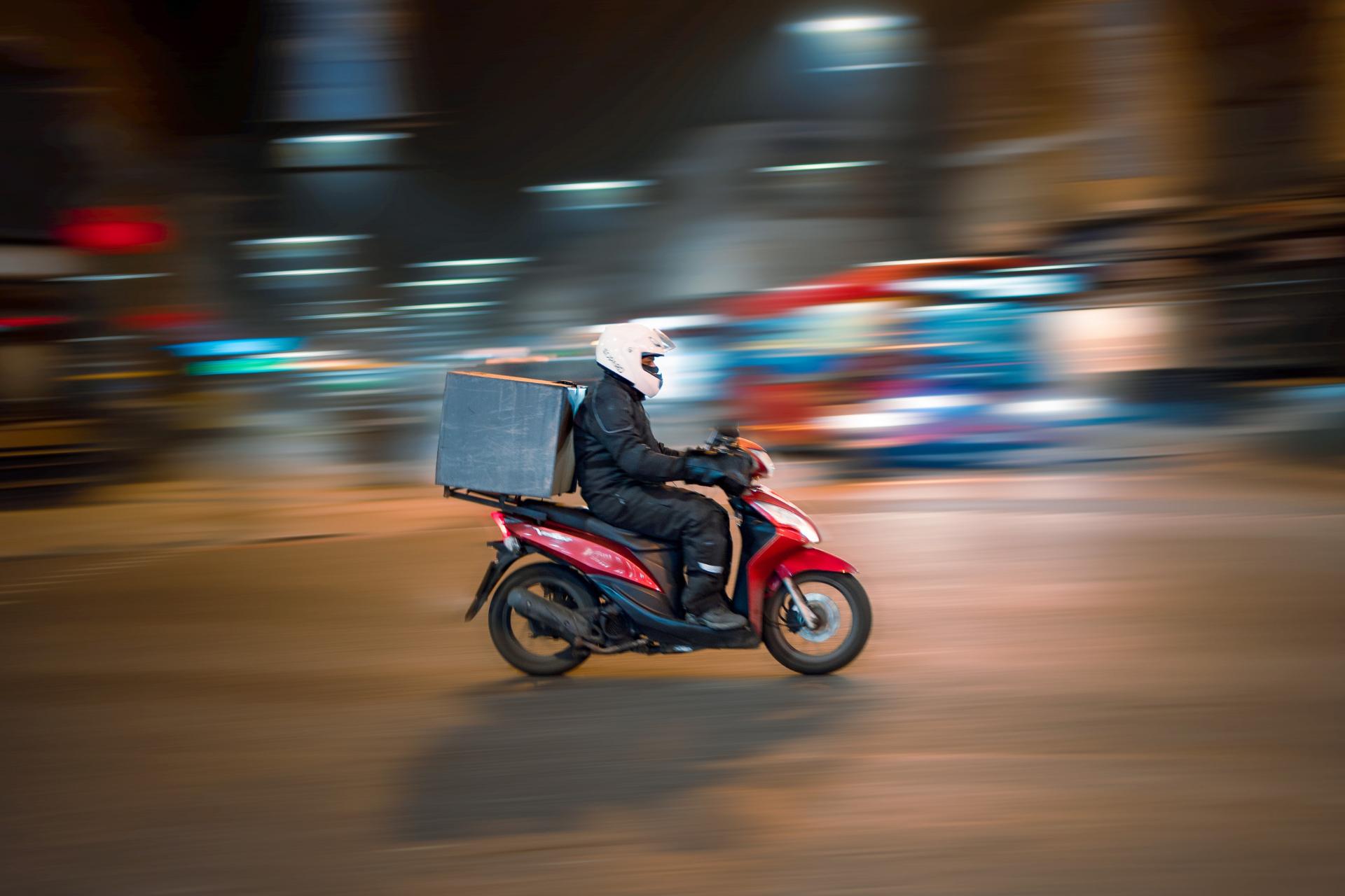Rapaz das entregas em uma vespa passando pela cidade